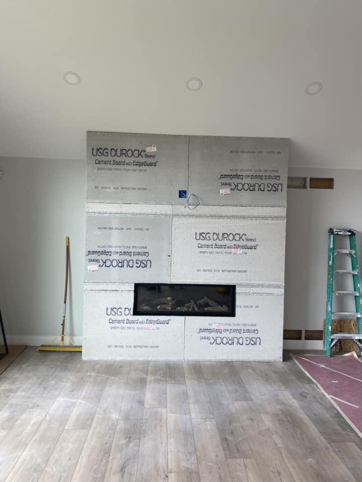Fireplace accent wall mid-construction with cement board sheets installed over stud framing around linear gas fireplace insert